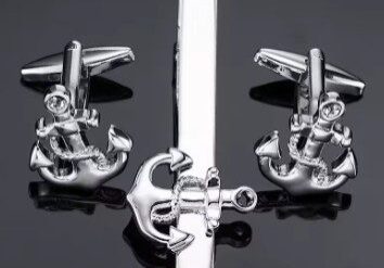 A tie clip and two anchor cufflinks on top of a black surface.