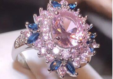 A pink diamond ring with blue sapphires on top of it.